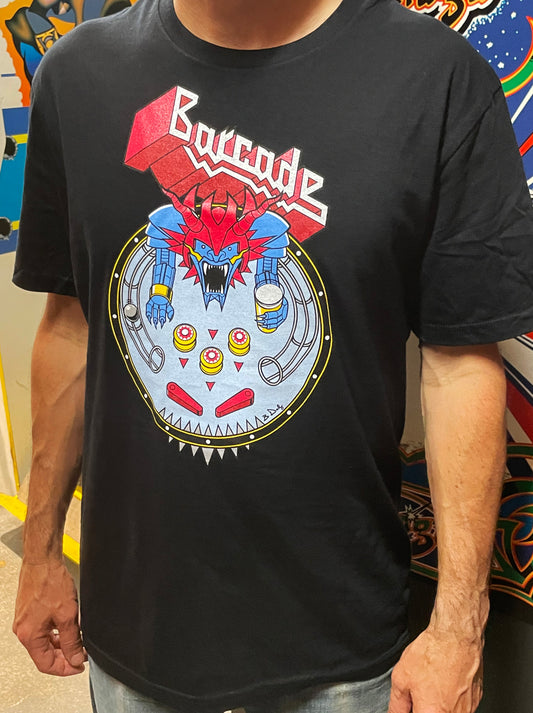 A person wearing a black short-sleeve graphic T-shirt with a large multicolor front print featuring the word 'Barcade' and a robot/mechanical character inside a circular design. The photo is cropped from the neck to the hips, with a store-like background visible behind the model.